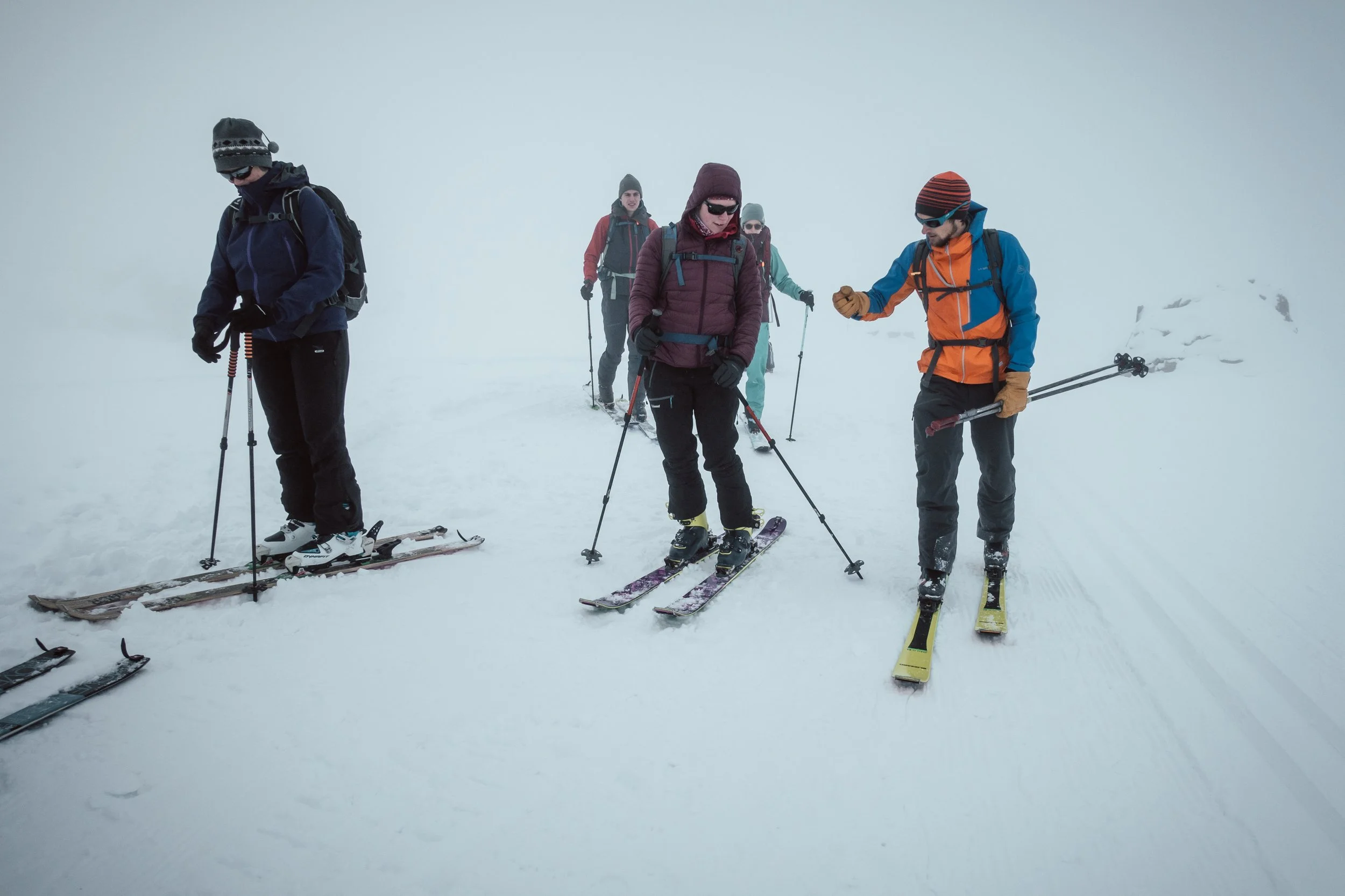 Fünf Menschen beim Skifahren in nebliger, verschneiter Berglandschaft.