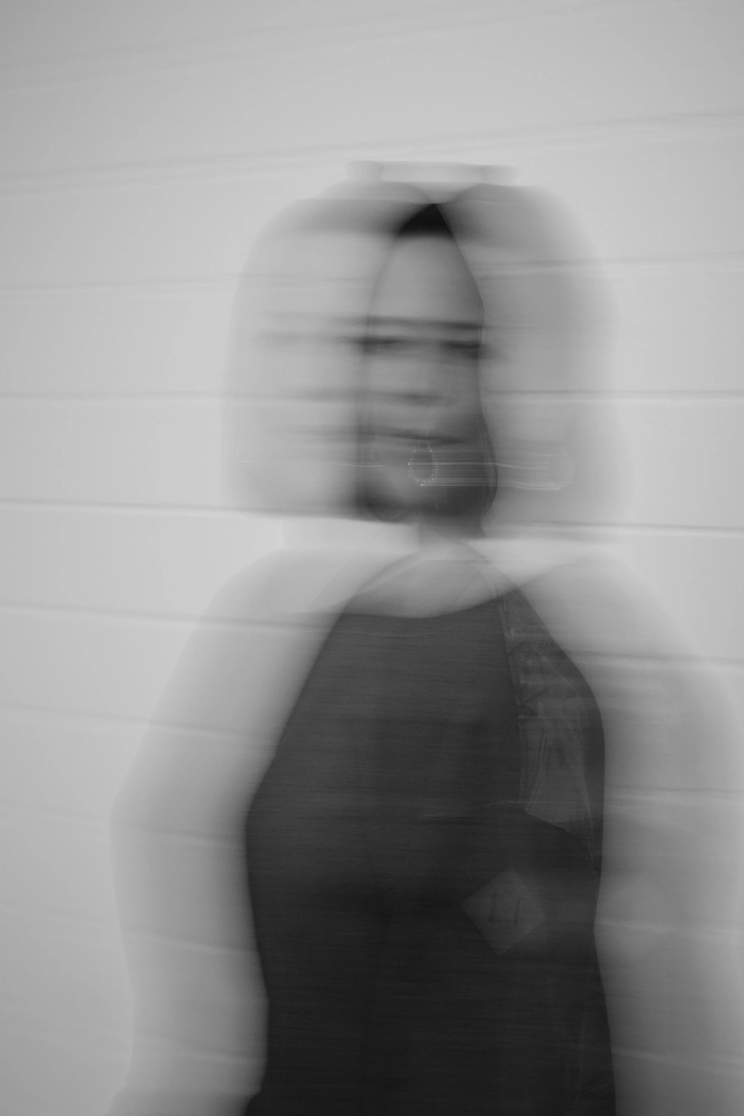 Schwarz-weiß-Fotografie eines verschwommenen Kopfporträts einer Frau mit Brille, vor einem hellen Hintergrund.
