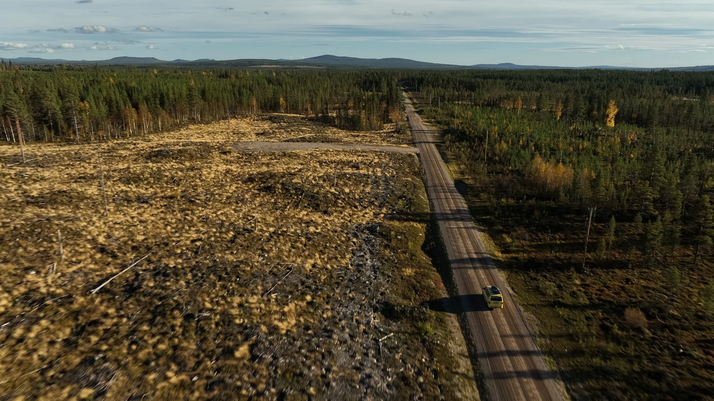 Luftaufnahme von einem ländlichen Waldgebiet mit einer unbefestigten Straße und einem Auto, die durch die Landschaft führt.