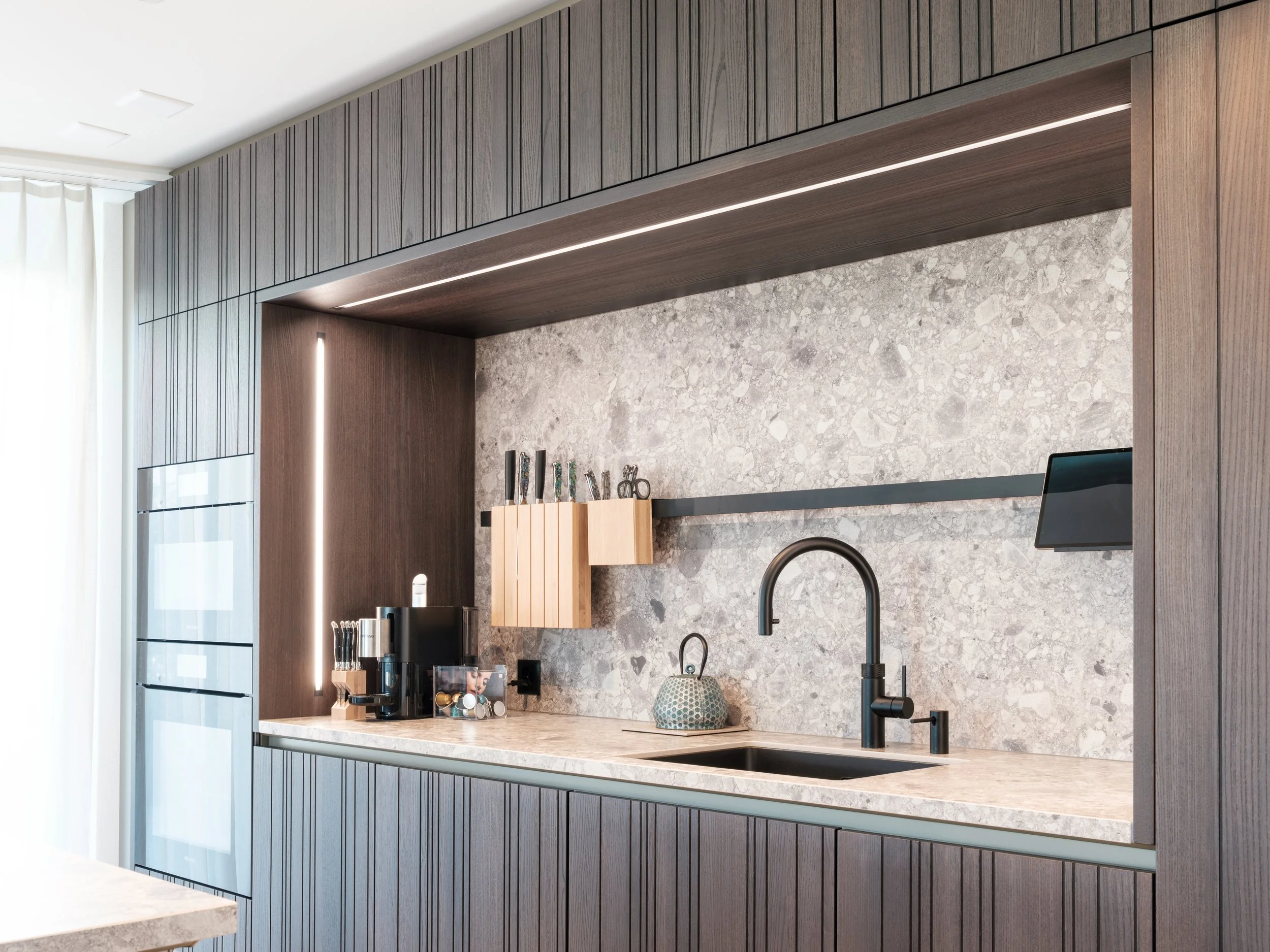 Moderne Küchenzeile mit schwarzen Armaturen, Kaffeemaschine, Holzregal, grauer Marmor-Wand und Holzpaneelen