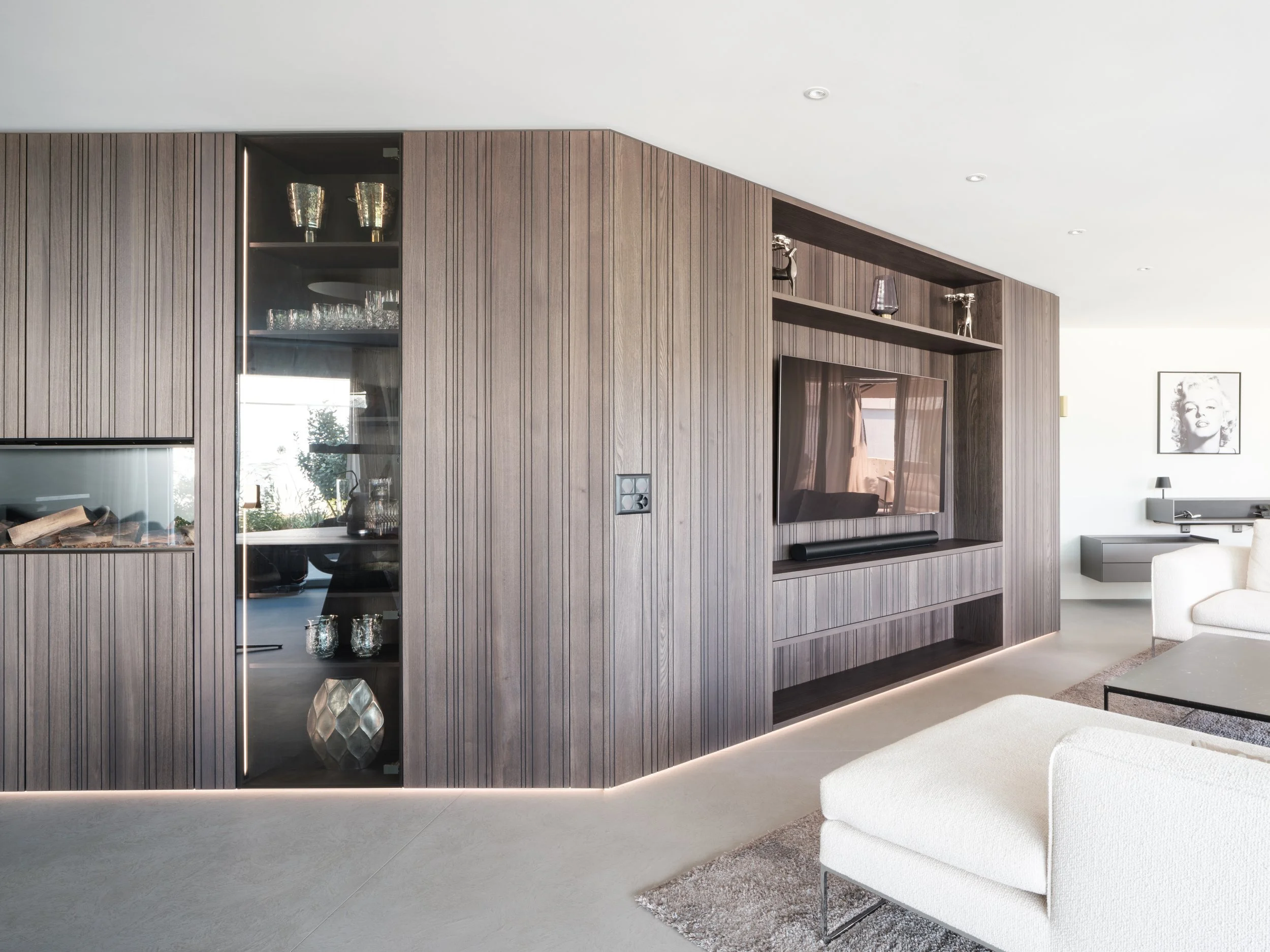 Moderner Wohnraum mit dunklem Holz-Nischenwand, eingebautem TV und weißen Polstermöbeln.