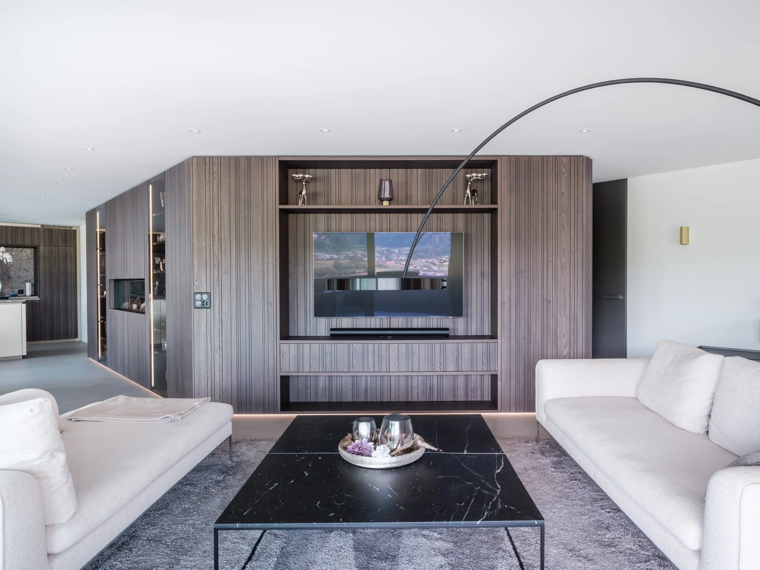 Modernes Wohnzimmer mit schwarzen Marmortisch, weißen Sofas und dunklem Holzregal mit Fernseher
