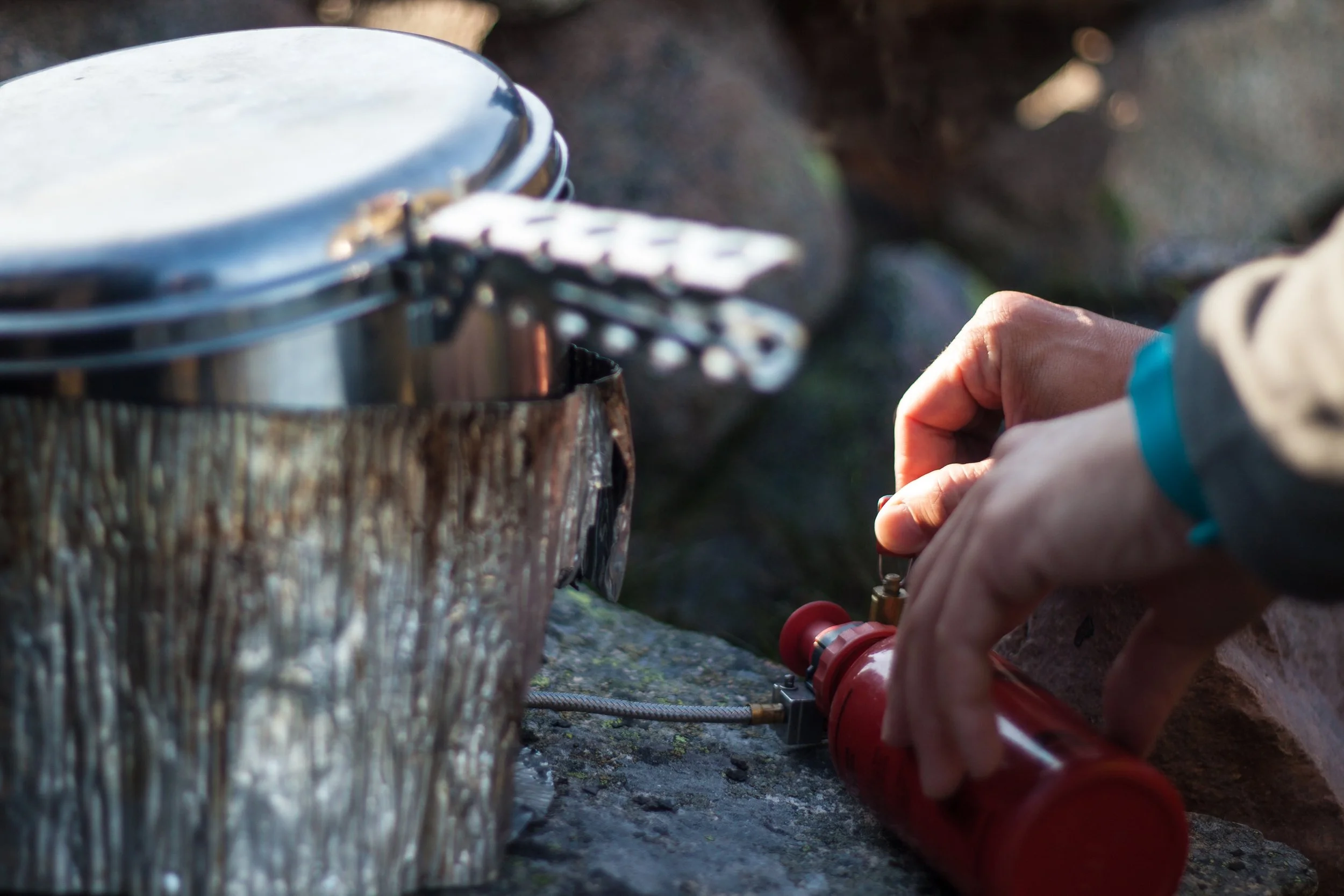 Person stellt eine kleine Flasche mit Gaszufuhr in eine große Edelstahlbox auf einem Felsen