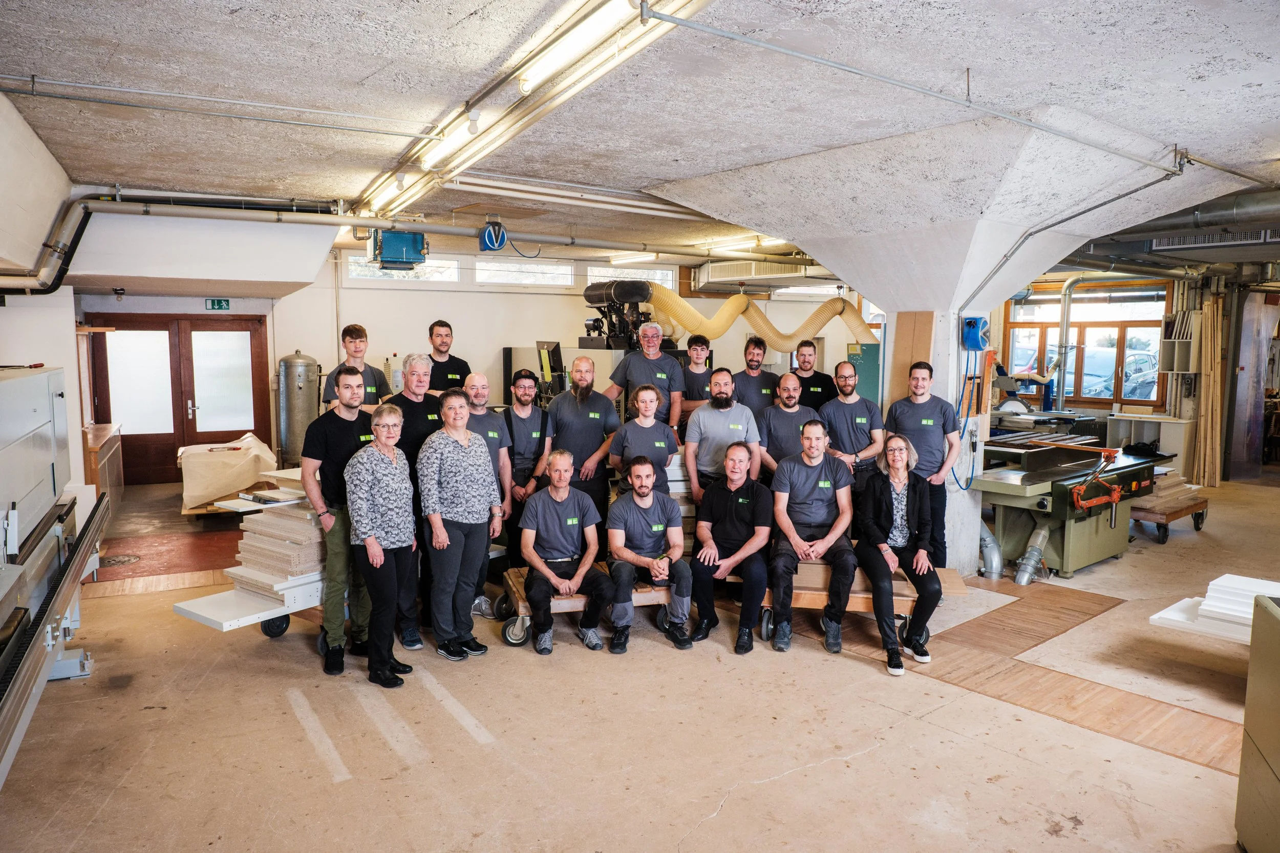 Gruppenfoto von Mitarbeitern in einer Werkstatt, umgeben von Holzarbeiten und Maschinen.