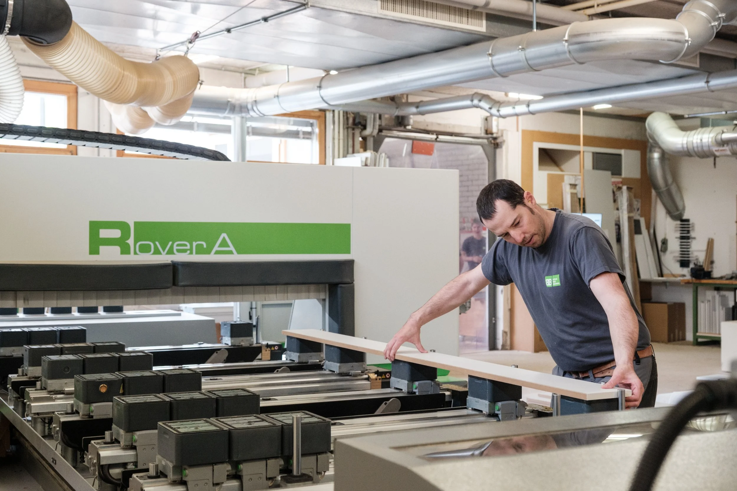 Mann arbeitet in einer Werkstatt mit einer CNC-Maschine, die mit dem Label "RoverA" versehen ist, beim Bearbeiten eines Holzstücks.