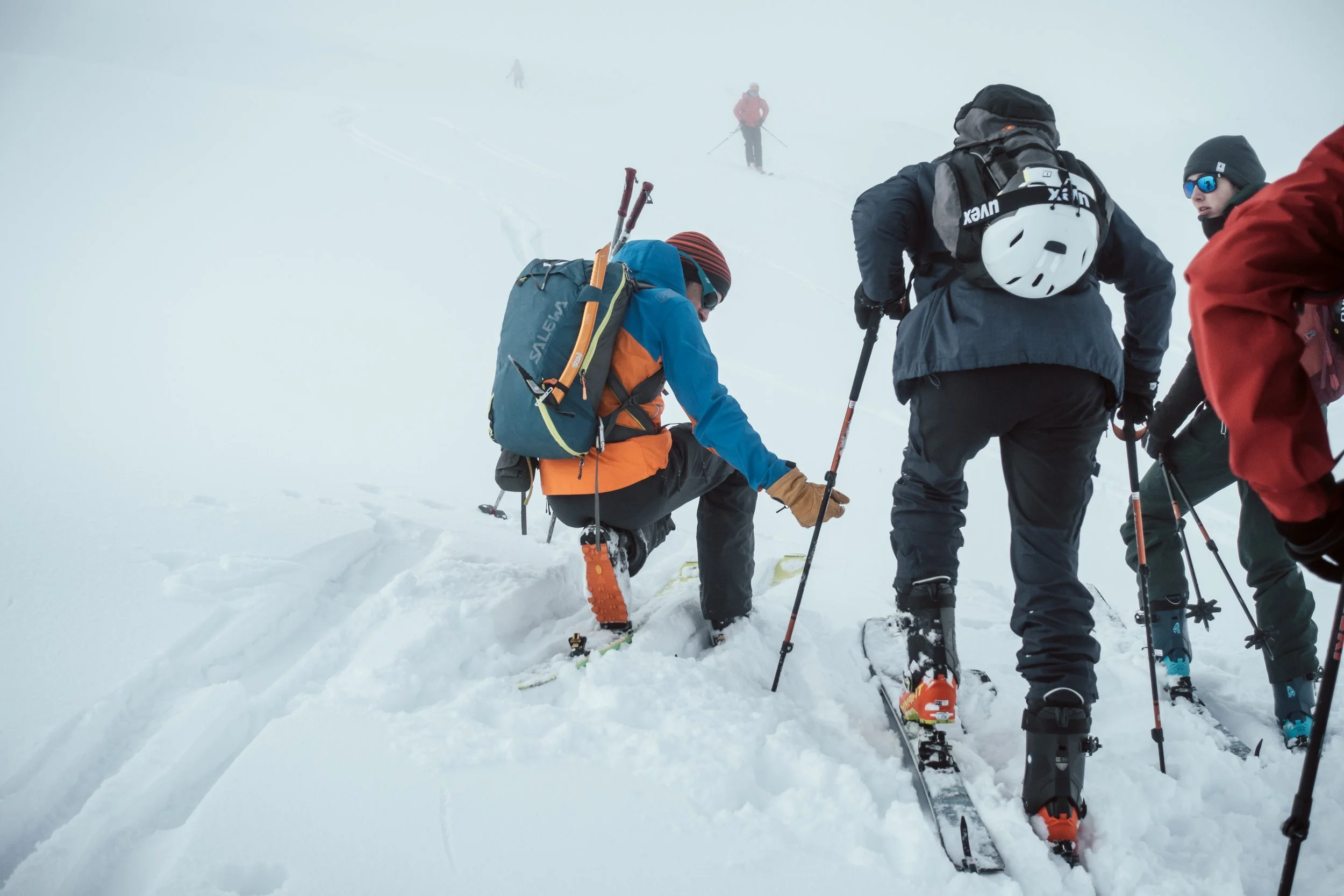 Gruppe von Skifahrern auf verschneitem Berg, einer hilft einem anderen beim Hochsteigen.