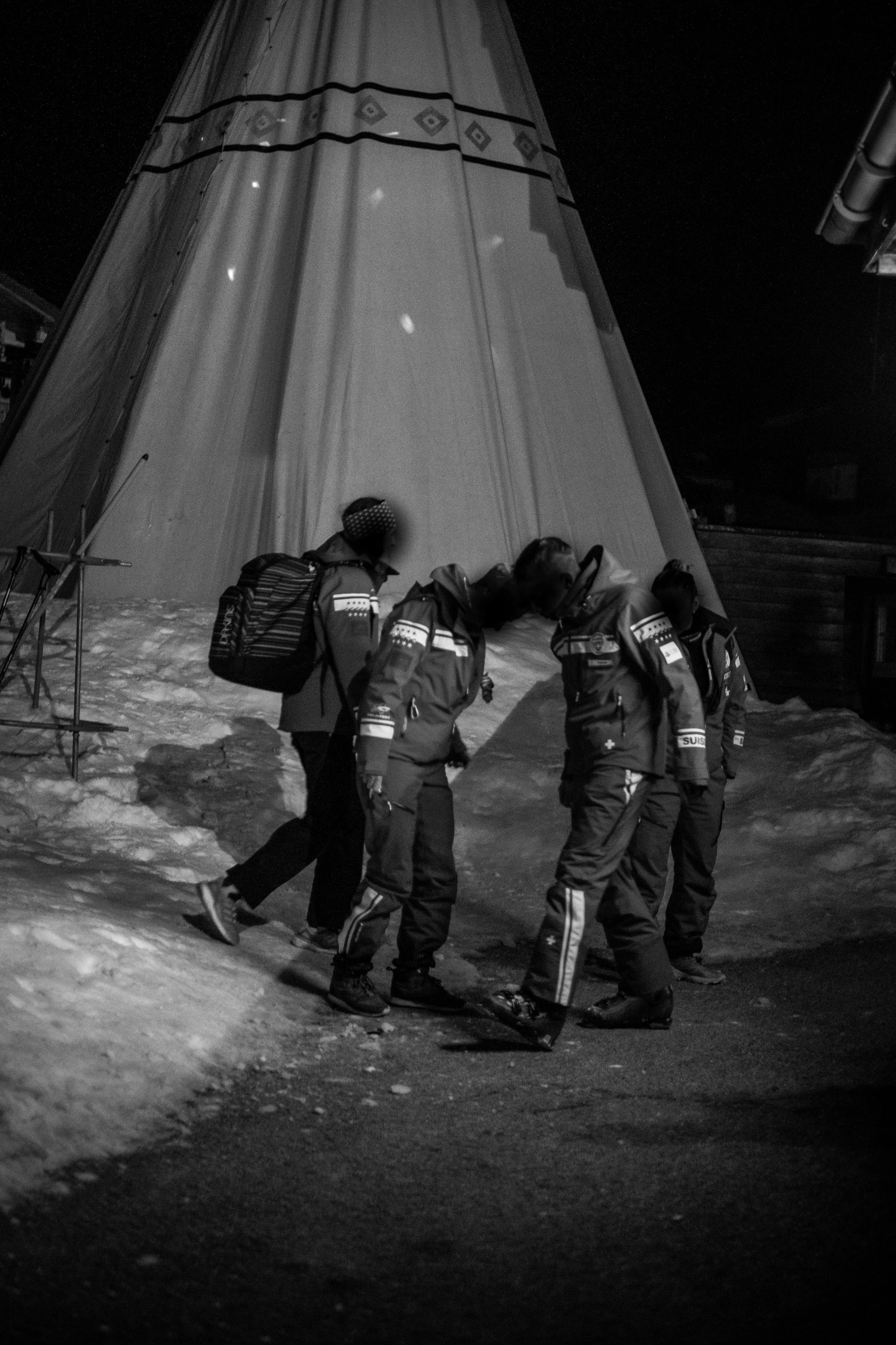 Vier Rettungskräfte in Winterkleidung stehen auf einer verschneiten Straße bei Nacht, vor einem großen Zelt.